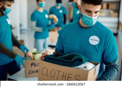 Young man working with volunteers in charitable foundation and carrying clothes in donation box.