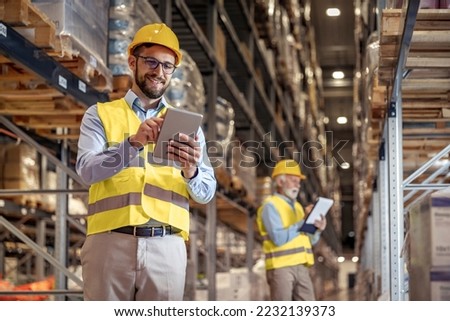 Young man working in warehouse and looking at tablet.