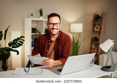 Young man works from home at a desk with a tablet and a laptop - Powered by Shutterstock