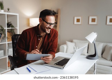 Young man works from home at a desk with a tablet and a laptop - Powered by Shutterstock