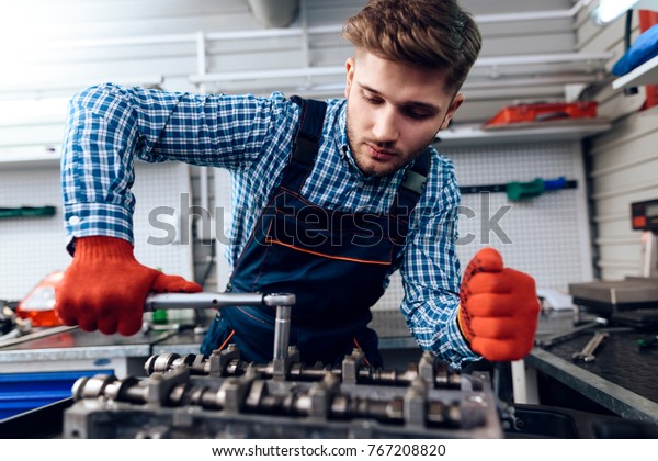 A young man works at a service station. The\
mechanic is engaged in repairing the car. The young mechanic is\
repairing the engine of the\
car.
