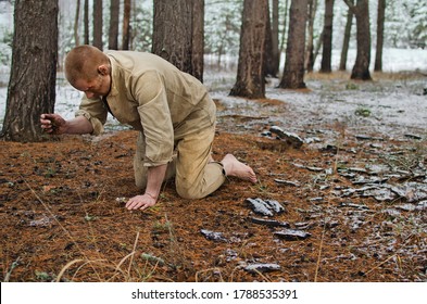 Young Man In A World War II Uniform And Barefoot Kneels In A Winter Forest