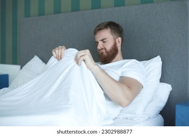 Young man worrying about his penis and erection failure, surprised guy is having trouble with his potency in bed in bedroom 