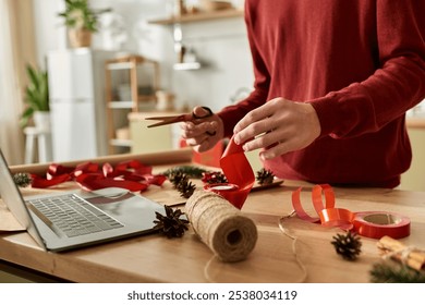 A young man wraps Christmas gifts in a warm kitchen with red ribbons and natural accents. - Powered by Shutterstock