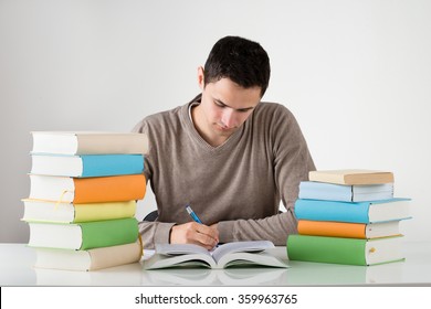 Young Man Writing In Book While Studying At Table Against White Background