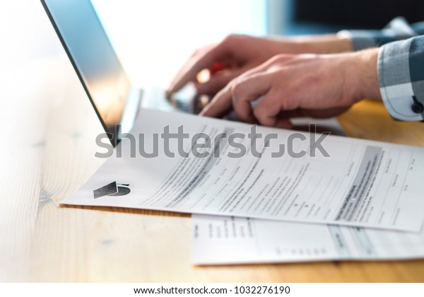 Young man writing college or university\
application form with laptop. Student applying to school.\
Scholarship document, admission paper or letter on table. Typing\
email. Education and\
communication.