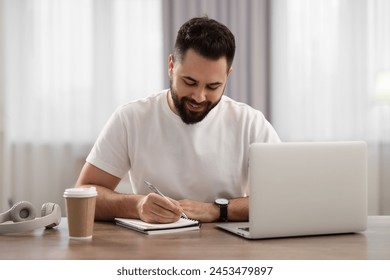 Young man writing down notes during webinar at table in room