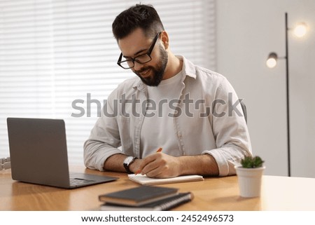 Young man writing down notes during webinar at table in room