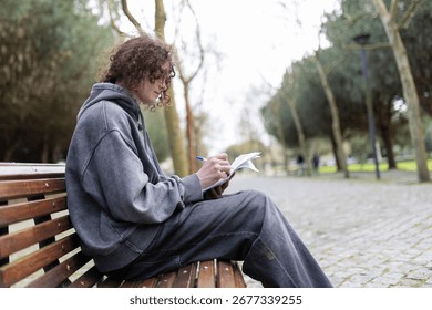 Young man writing in notebook while sitting on park bench