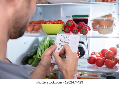 Young Man Writing Shopping List Near Open Refrigerator
