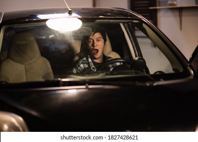 A Young Man Yawns At The Wheel Of An Old Black Car Parked In The Garage