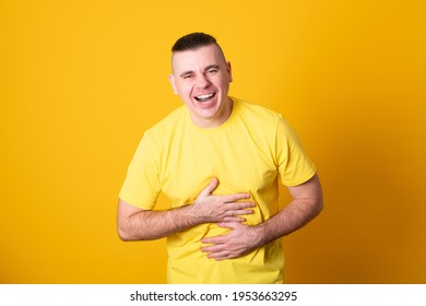 Young Man In A Yellow Shirt Holding His Stomach Laughing On Yellow Background. 