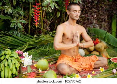 Young man in a yoga position surrounded by tropical fruits and flowers in an exotic garden.