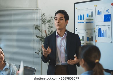 Young manager explaining charts and graphs on whiteboard during a presentation to his team in the office