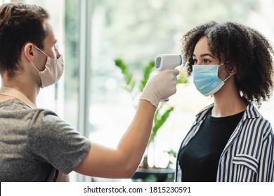 Young manager in protective mask and gloves checking temperature on client forehead at beauty salon, side view - Powered by Shutterstock