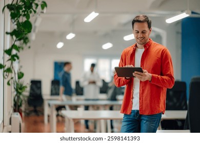 Young manager smiling while using a digital tablet in a modern office, with colleagues engaged in work in the background, highlighting the blend of technology and business