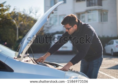 Young man's car breaks down. He gets very angry and tries to fix it.