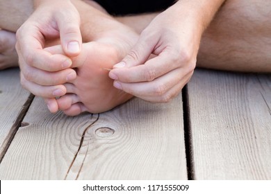 Young man's hand removing wooden splinter from foot. Accident on wooden floor after walking by barefoot. Front view. Close up.
