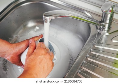 Young man's hands washing a white cup with water and dish soap. Close up shot of a man's hands rinsing a cup that was dirty and used. Concept of cleanliness