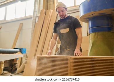 Young manual worker in uniform standing at stack with thin wooden boards during his work at furniture factory