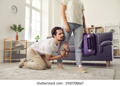Young married couple breaking up. Angry woman leaving home with packed suitcase. Clingy desperate husband on floor holding wife's leg begging his love to stay. Relationship breakup and divorce concept