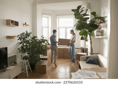 Young married couple carrying boxes into rented flat, cozy room with houseplants, moving into new home after renovation, buying apartment, enjoying relocation. Full length shot - Powered by Shutterstock