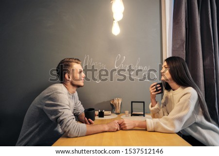 Young married couple in casual clothes, man and woman, sitting at home in the kitchen at the table. They drink tea and talk. Soul communication and home comfort.