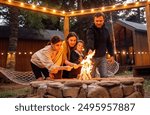 A young married couple with children roasts marshmallows on the fire. A man with his wife, son and daughter are having fun in the backyard of the house. A happy family outdoors near a campfire