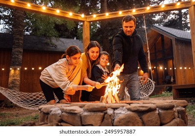 A young married couple with children roasts marshmallows on the fire. A man with his wife, son and daughter are having fun in the backyard of the house. A happy family outdoors near a campfire - Powered by Shutterstock