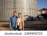 A young married couple and an elevator with grain. Husband and wife farmers in casual clothes at a wheat storage warehouse. An attractive woman and a man work on a farm