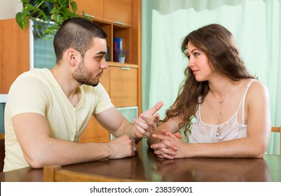 Young married couple having serious talking at the table in home