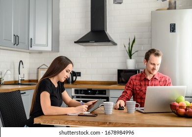 Young married couple in the kitchen, wife with a tablet, husband with a laptop. Concept of lifestyle, technology.