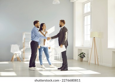 Young married couple make deal, buy new house and exchange handshake with relator. Happy man and woman standing in modern light spacious light living room and shaking hands with real estate agent - Shutterstock ID 2276680811