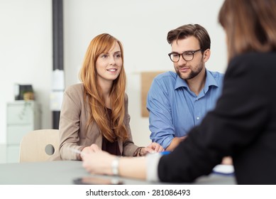 Young Married Couple In A Meeting With A Broker Or Agent With Focus To The Attractive Redhead Wife