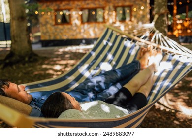 A young married couple is relaxing in the backyard of the house. An attractive husband and wife are lying in a hammock outside. A happy family spends time together and enjoys their holidays - Powered by Shutterstock