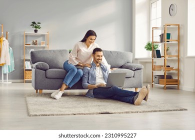 Young married couple sitting on sofa in the living room at home using tablet PC for internet and social media. Happy family resting on couch enjoying weekend watching video or talking on video call. - Powered by Shutterstock