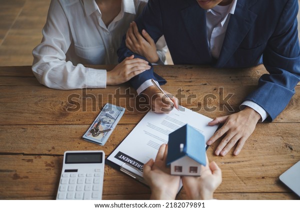 Young married couple talking to a real\
estate agent to sign a house purchase\
contract.
