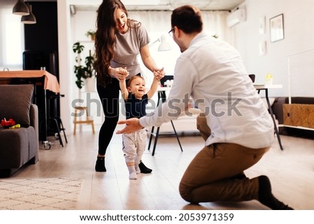 Young married couple teaching their son to learn the first baby steps in their home