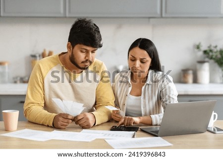 Young married indian couple have financial difficulties, sitting at table at kitchen at home, using computer and calculator, calculating spendings and income, paying bills online