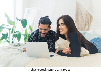 Young Married Millennial Couple Lying Down On Bed In Their Fresh Modern Bedroom And Watching Something On A Laptop. Wireless Technology And Entertainment Concept. High Quality Photo