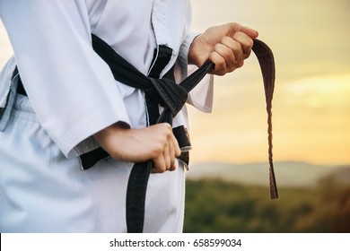 A young martial arts master knots a black belt. Close-up. Image with the effect of sunlight. - Powered by Shutterstock