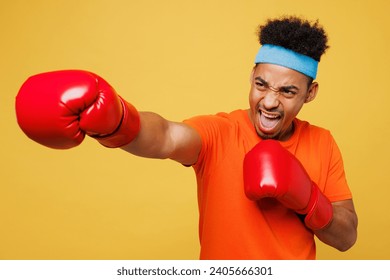 Young masculine fitness trainer instructor sporty man sportsman wear orange t-shirt boxing red gloves punch spend time in home gym isolated on plain yellow background. Workout sport fit abs concept - Powered by Shutterstock