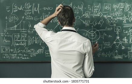 Young mathematician solving problems and writing formulas on the chalkboard, back view