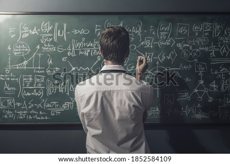 Young mathematician solving problems and writing formulas on the chalkboard, back view