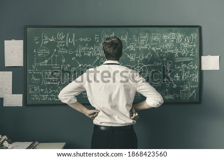 Young mathematician solving problems and writing formulas on the chalkboard, back view