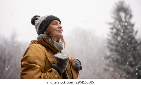 Young mature adult caucasian woman in a hat and yellow jacket breathing fresh air in the winter forest - Shutterstock ID 2204153585