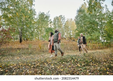 Young and mature couples in stylish warm casualwear moving down road in the forest among trees with green and yellow leaves