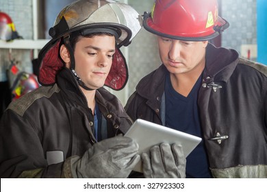 Young And Mature Firemen Using Tablet Computer At Fire Station