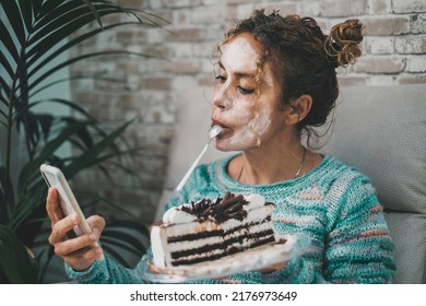 Young Mature Woman Using Mobile Phone At Home Eating An Ice Cream Cake. White Beauty Cream Treatment On Face. Indoor Leisure Female People Activity.. Lady Eating Tasty Food And Having Relax Indoor