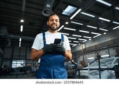 Young mechanic in blue overalls uses smartphone while surrounded by vehicles in workshop. - Powered by Shutterstock